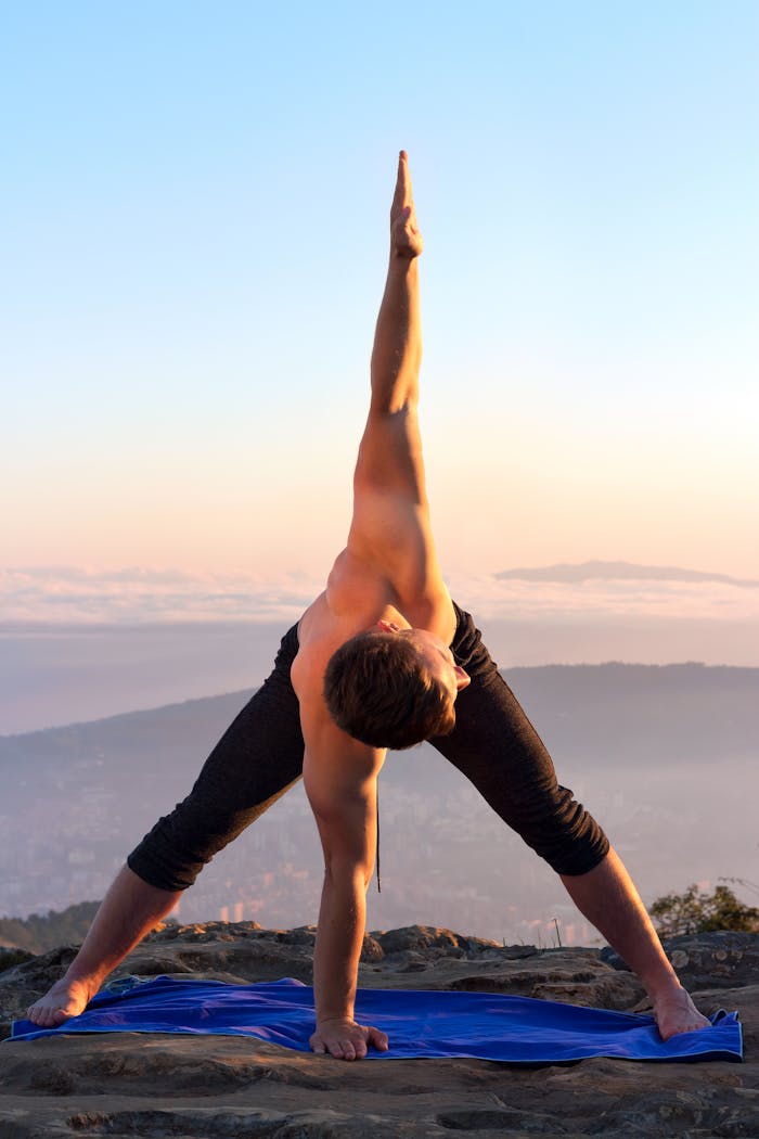 A man performing a yoga pose outside at sunrise, focusing on balance and flexibility.